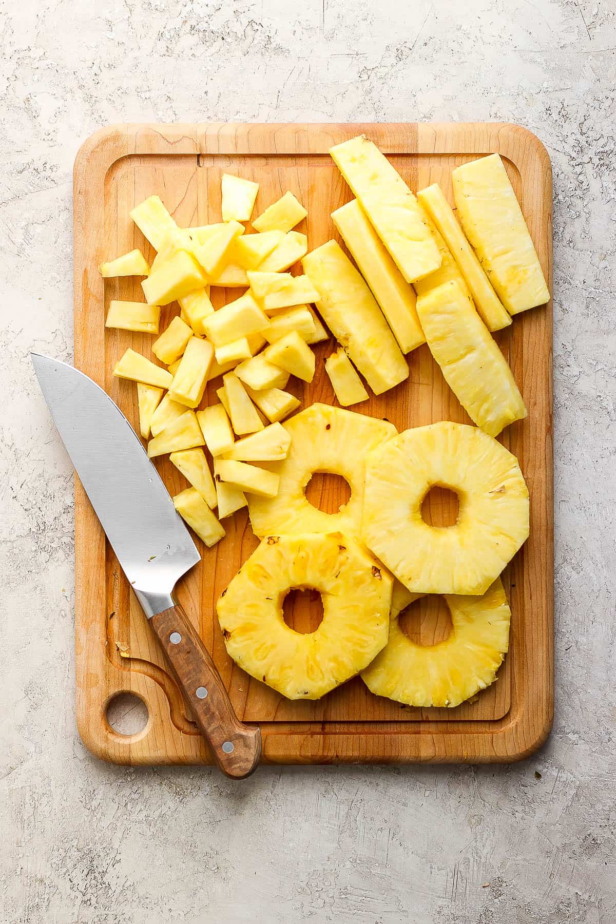 A wooden cutting board with pineapple rounds, strips, and chunks.