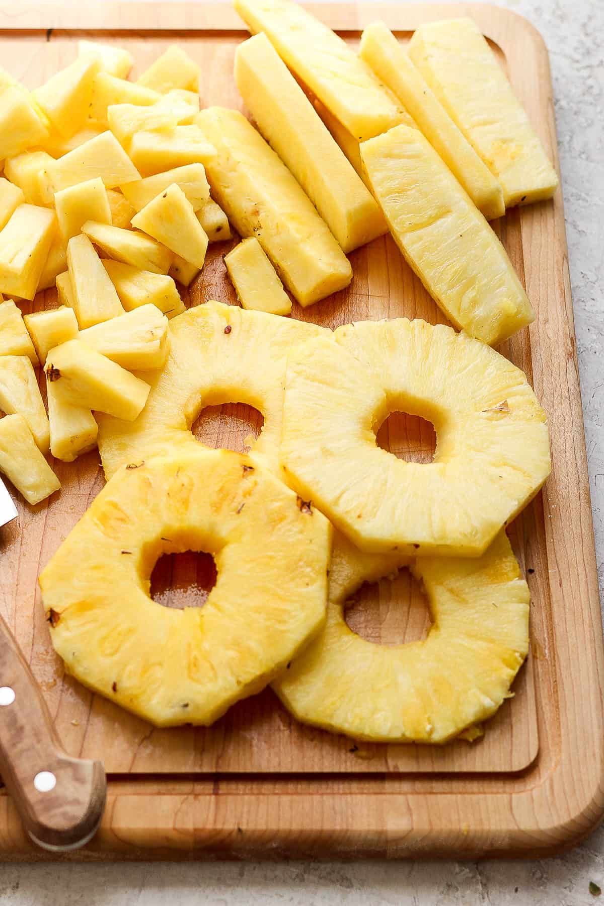 Pineapple rounds, strips, and chunks on a wooden cutting board.