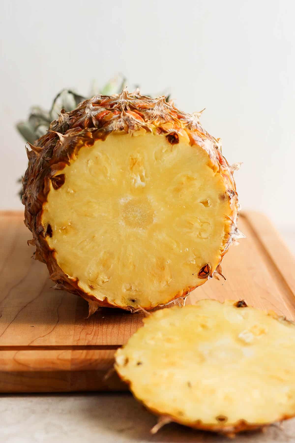 A pineapple on it's side on a wooden cutting board with the end cut off.