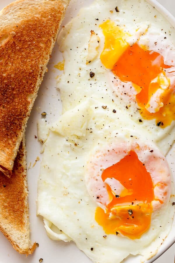 Someone holding a plate with two over easy eggs, a gold fork and a piece of toast.