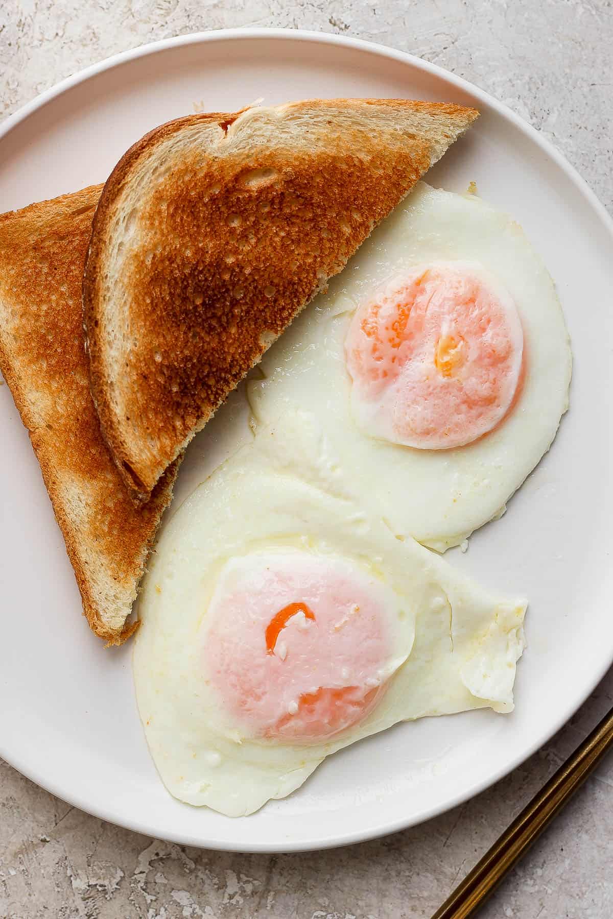 Two eggs over easy on a plate with two slices of bread.