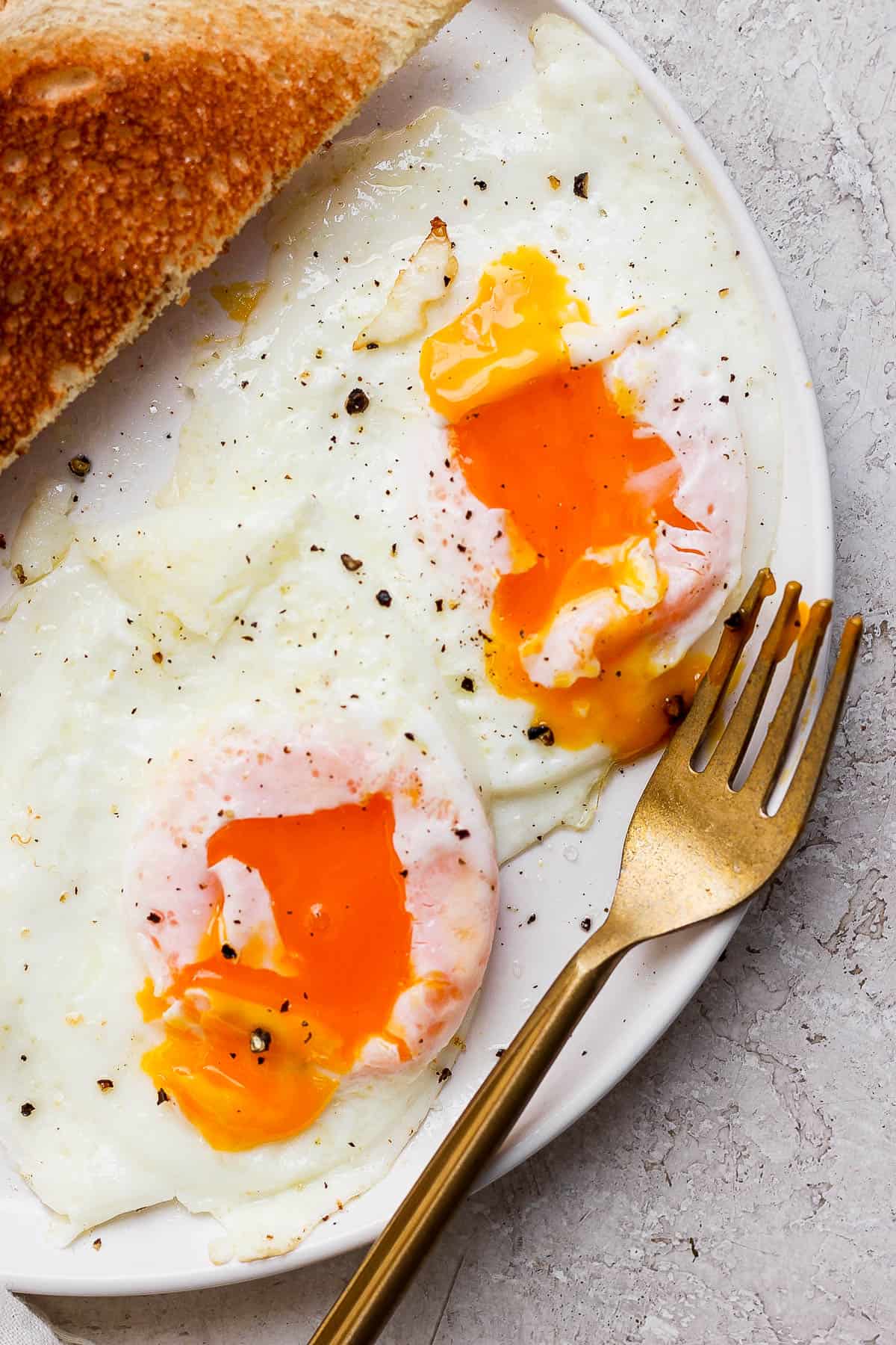Two eggs over easy on a plate with a fork and toast.
