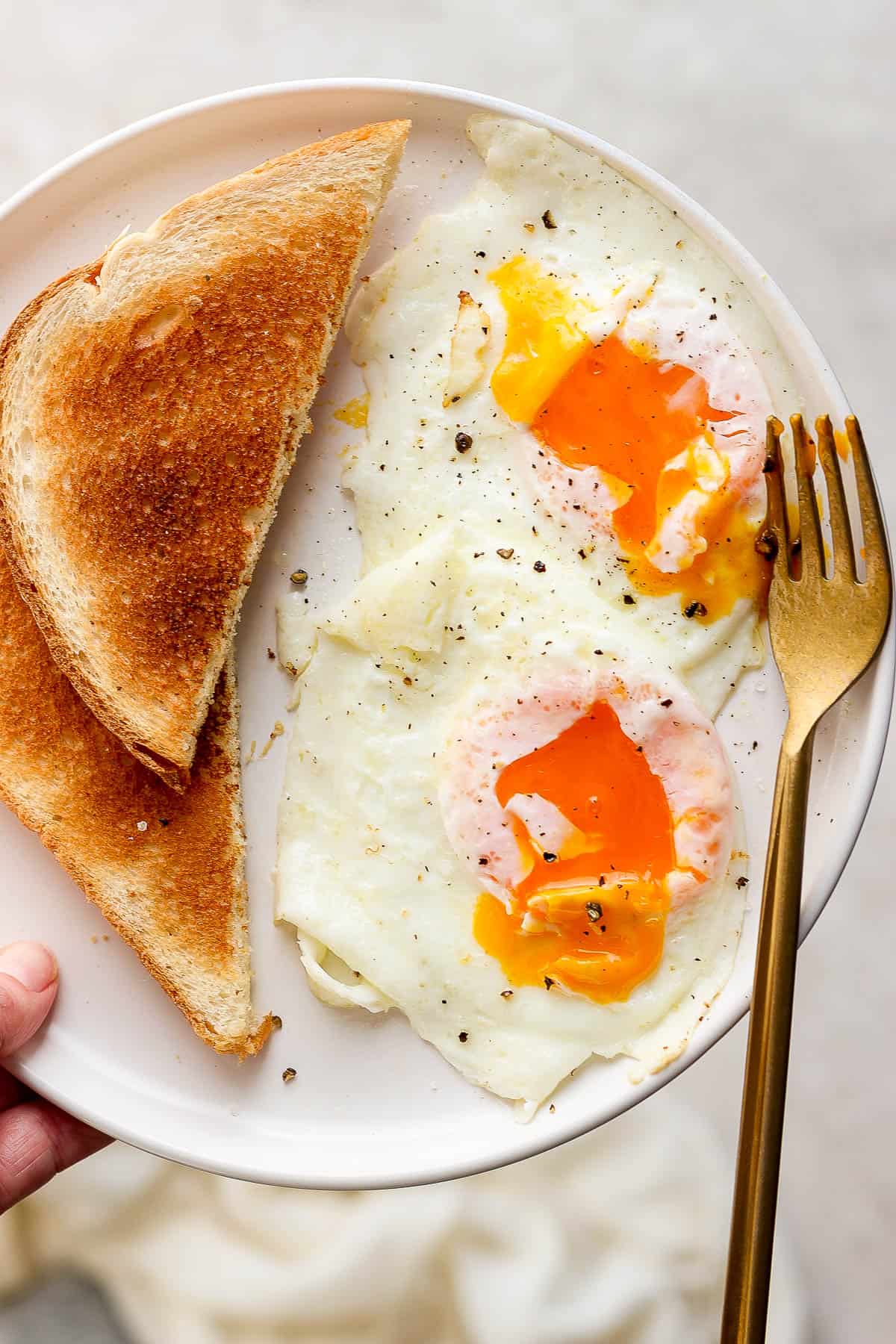 A plate with two eggs over easy with two pieces of toast and a fork.