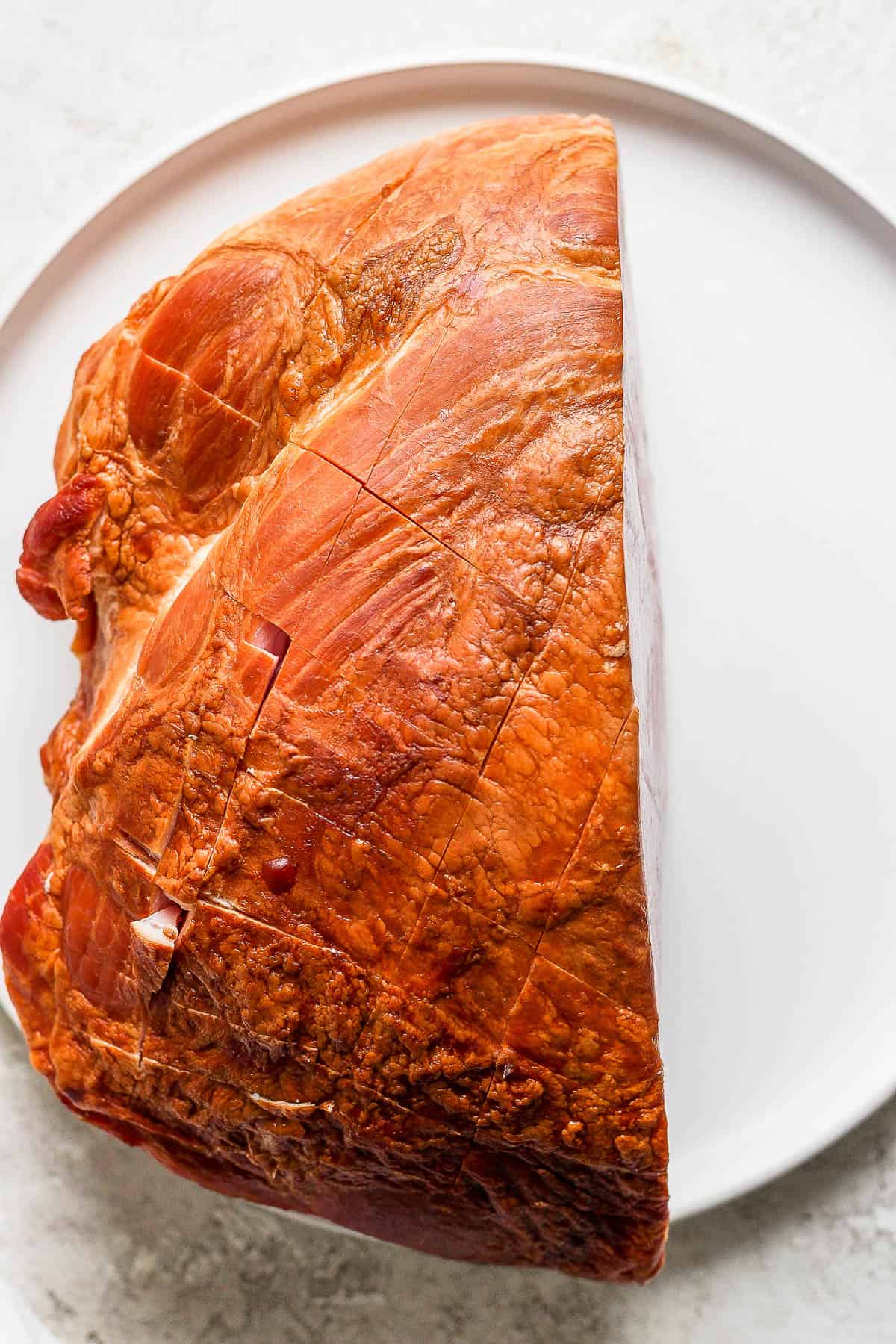 A scored ham on a large white plate.