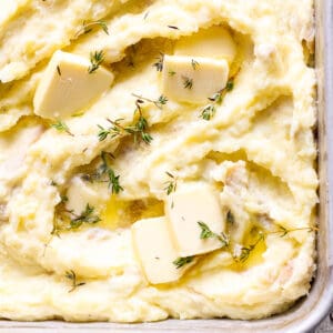 Top down shot of the corner of a pan of make ahead mashed potatoes with butter and fresh thyme on top.