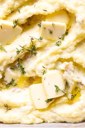 Top down shot of the corner of a pan of make ahead mashed potatoes with butter and fresh thyme on top.
