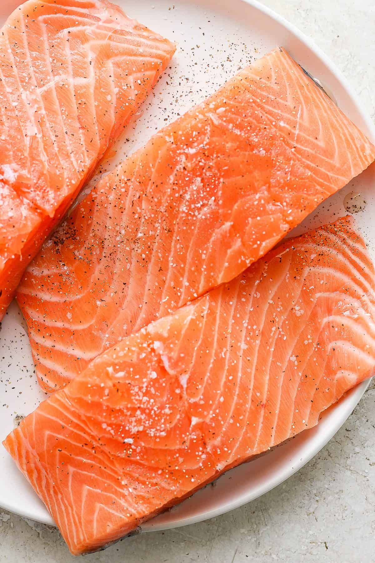 Raw salmon covered in oil, salt, and pepper on a plate.