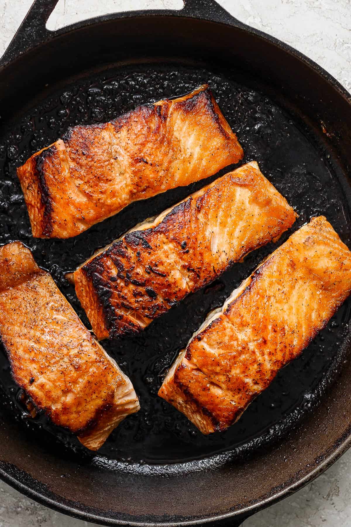 Salmon fillets in a skillet after being flipped and the skin-side is now down.