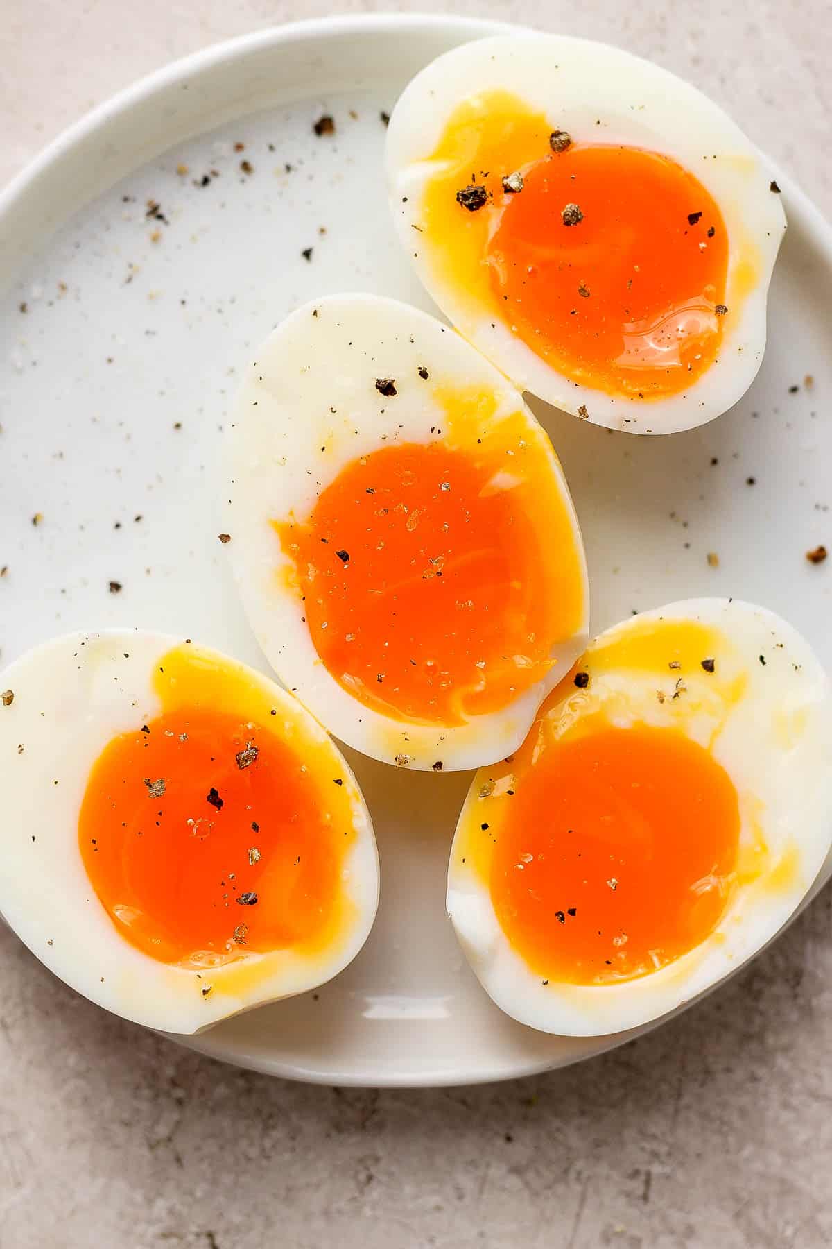 Two, 6-minute eggs peeled and cut in half on a plate with some cracked pepper on top.