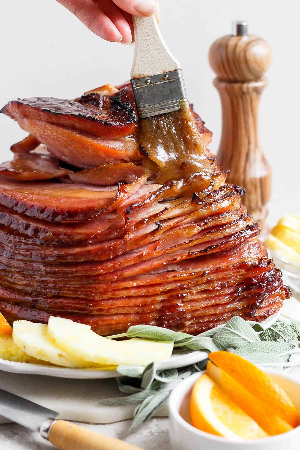 A cooked spiral ham on a plate being brushed with glaze.