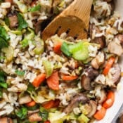 Top down shot of a wooden spoon sticking out of a pan of wild rice pilaf with carrots, celery and chopped parsley.