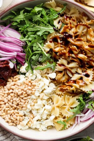 Top down shot of a bowl of balsamic pasta salad with pine nuts, gorgonzola cheese, pine nuts, argula and red onion.