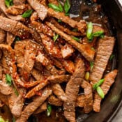 Top down shot of some cooked Beef Bulgogi in a cast iron skillet with sauce and green onions on top.