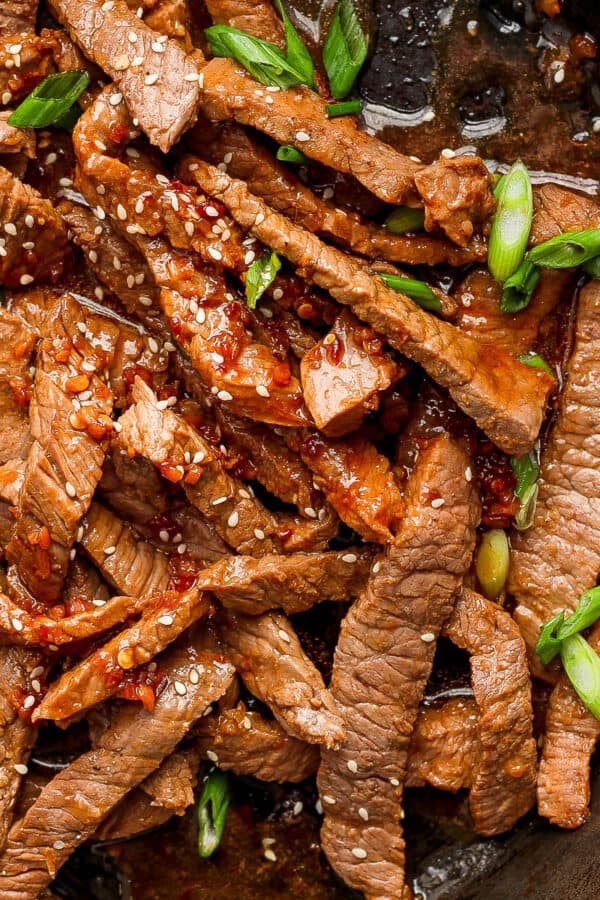 Top down shot of some cooked Beef Bulgogi in a cast iron skillet with sauce and green onions on top.
