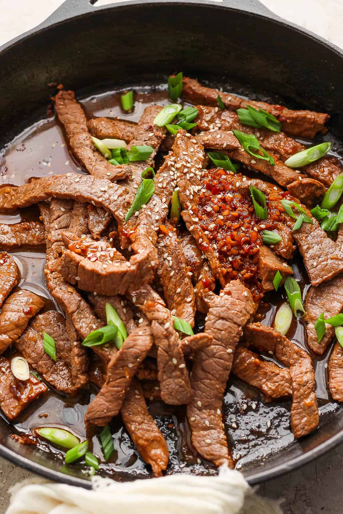 Beef bulgogi in a skillet topped with sliced green onions.