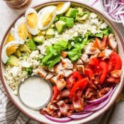 Top down shot of a big bowl of cobb salad with ranch dressing, bacon, red onion, roma tomatoes, chicken, blue cheese, avocado and hard boiled egg.