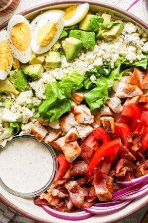 Top down shot of a big bowl of cobb salad with ranch dressing, bacon, red onion, roma tomatoes, chicken, blue cheese, avocado and hard boiled egg.