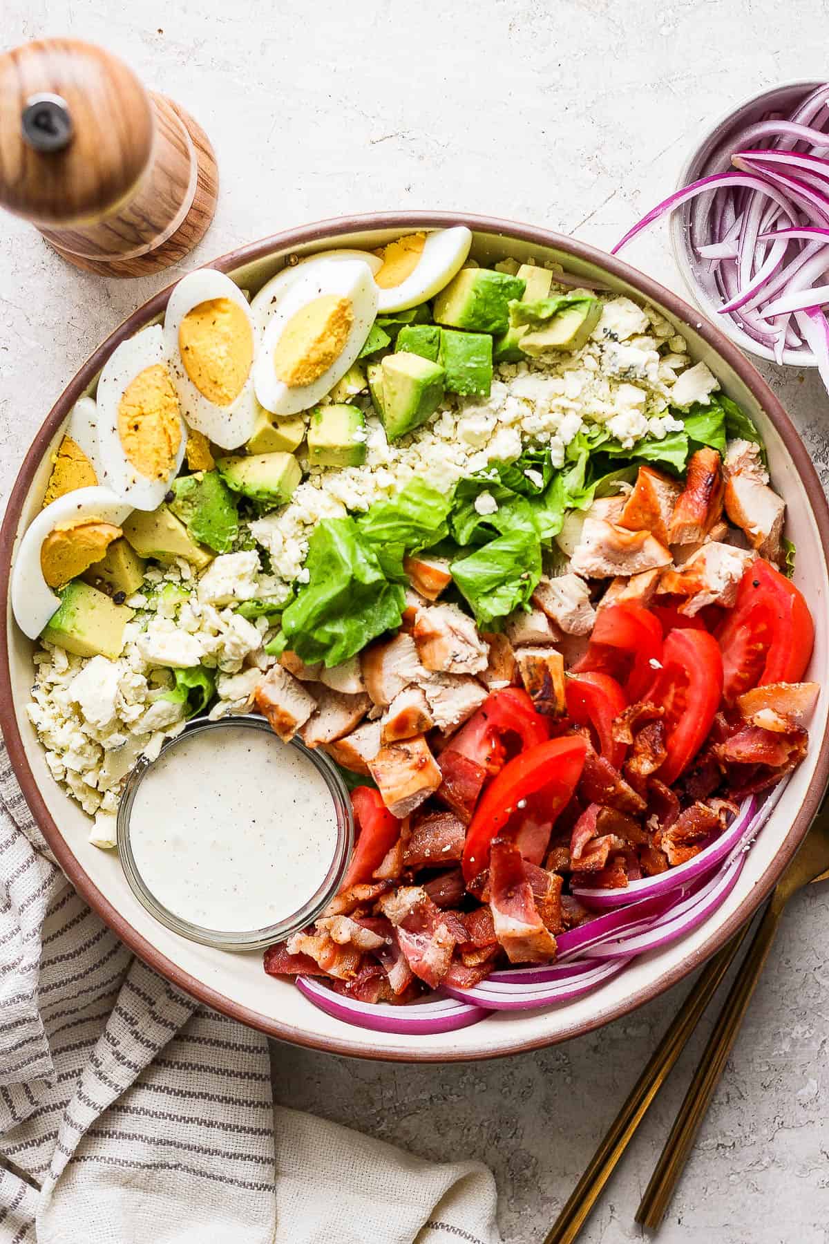 A cobb salad in a large bowl with a small bowl of herby ranch dressing nestled off to one side.