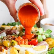 Someone pouring homemade French dressing on top of a Chef Salad.