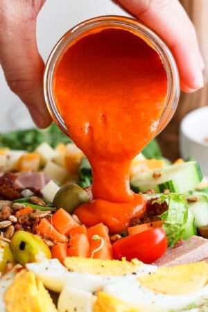Someone pouring homemade French dressing on top of a Chef Salad.