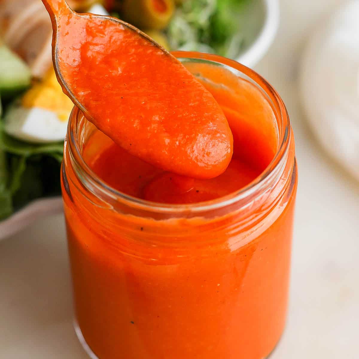 A jar of homemade French dressing with a spoon pulling some out.