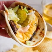 Someone holding a smash burger taco with shredded lettuce, burger sauce and pickles.