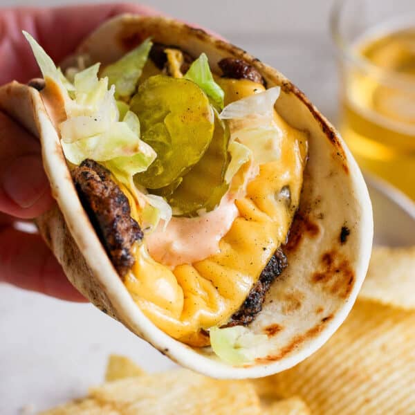 Someone holding a smash burger taco with shredded lettuce, burger sauce and pickles.