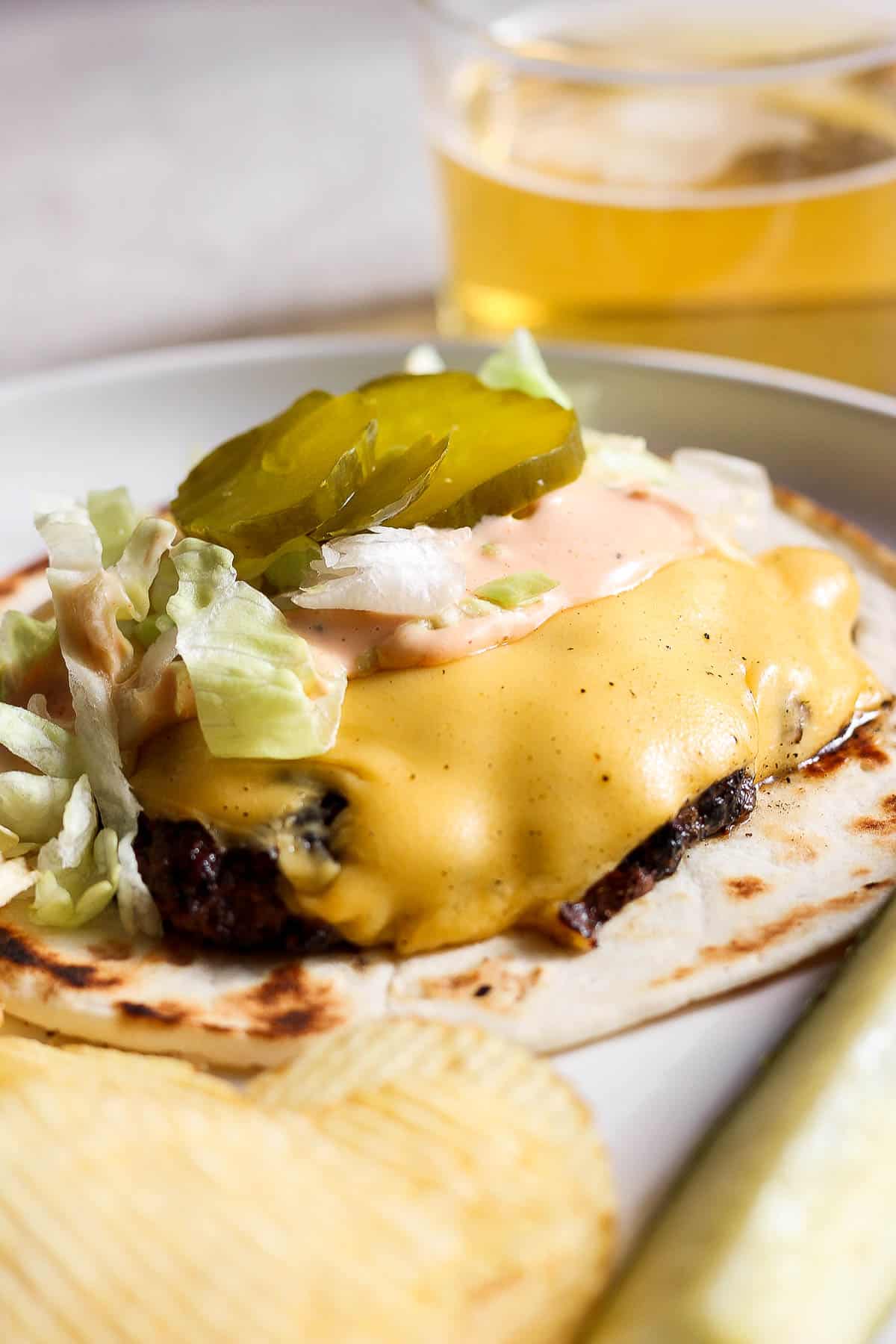 The tortilla, burger patty, cheese, burger sauce, lettuce, and pickles are on a plate.