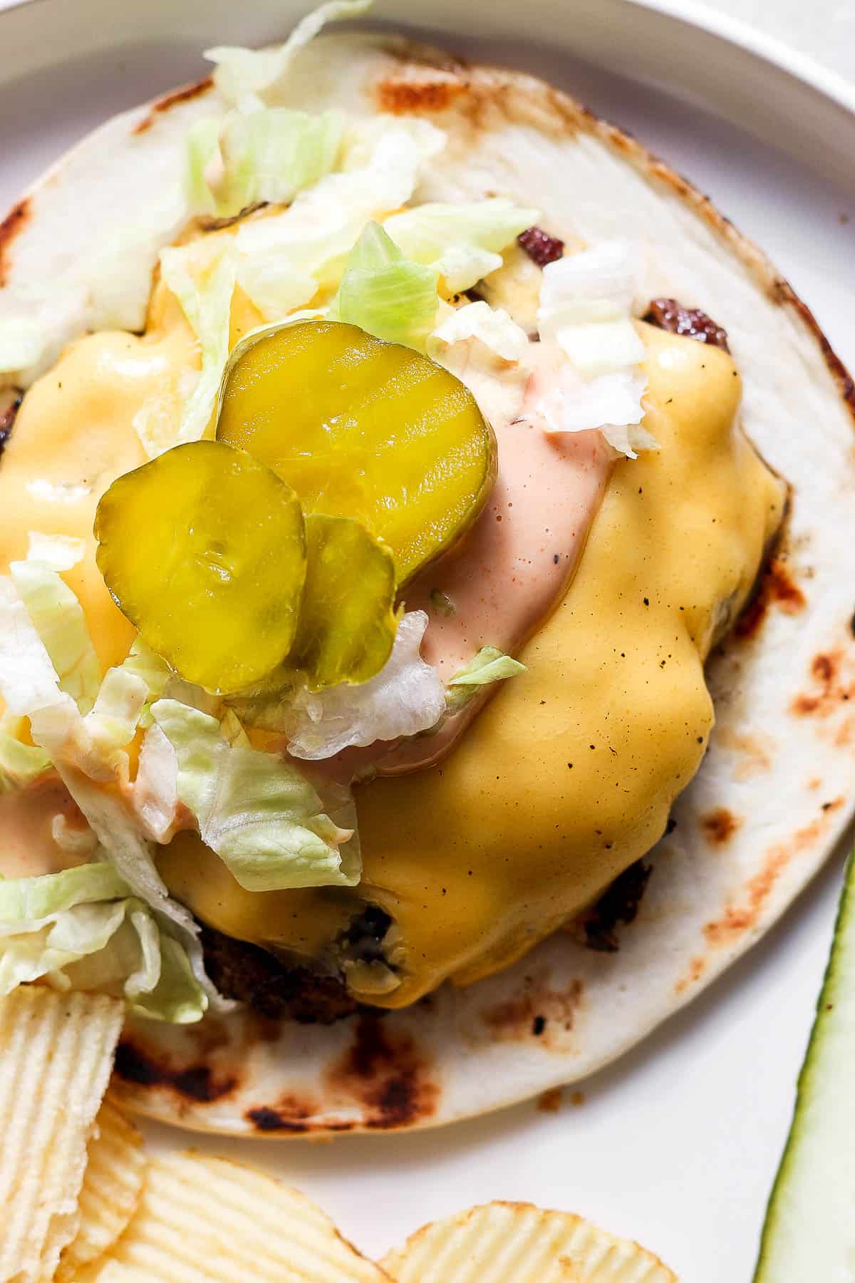 Smash burger taco topped with burger sauce, lettuce, and pickles.