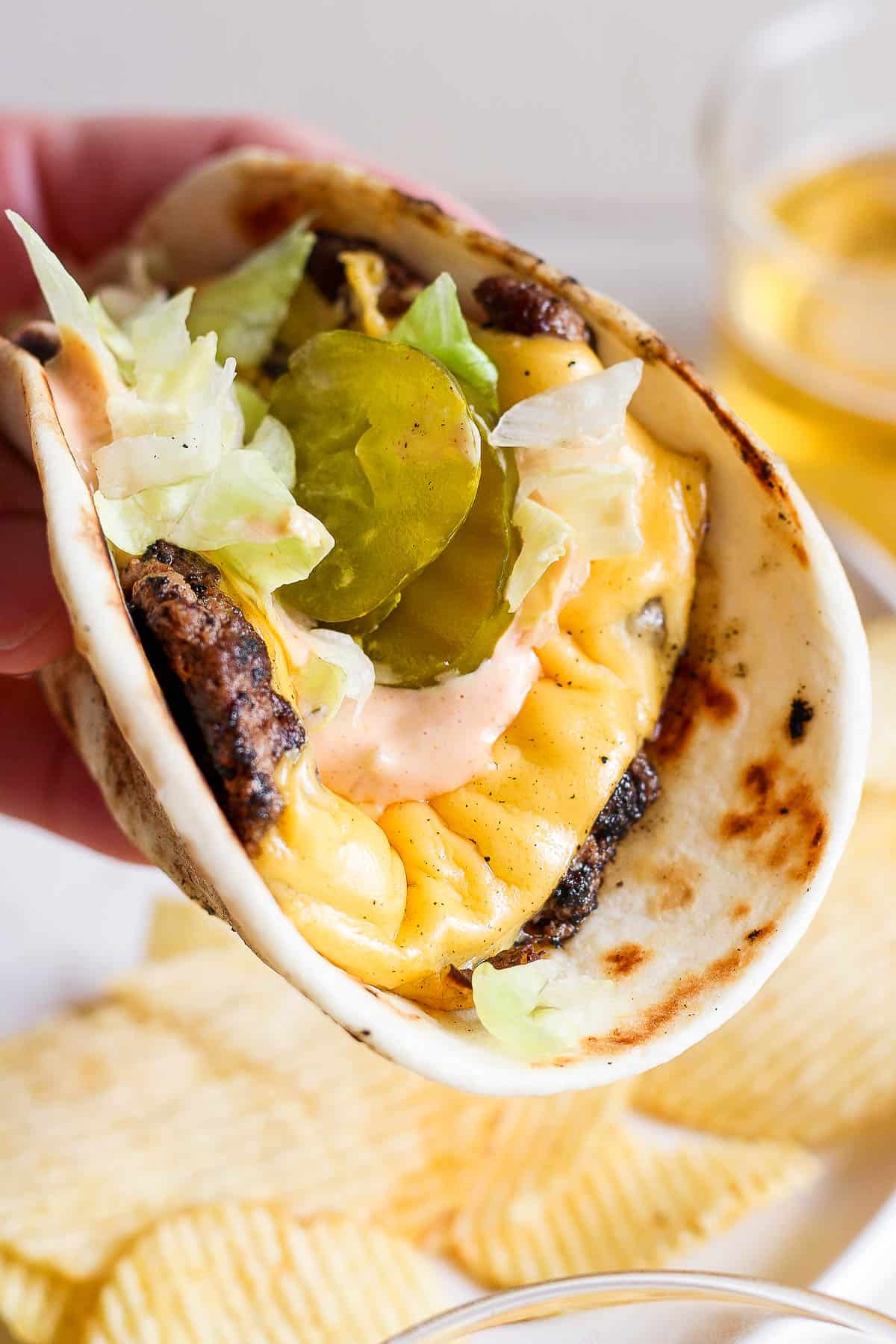 A hand holding a fully topped smash burger taco.