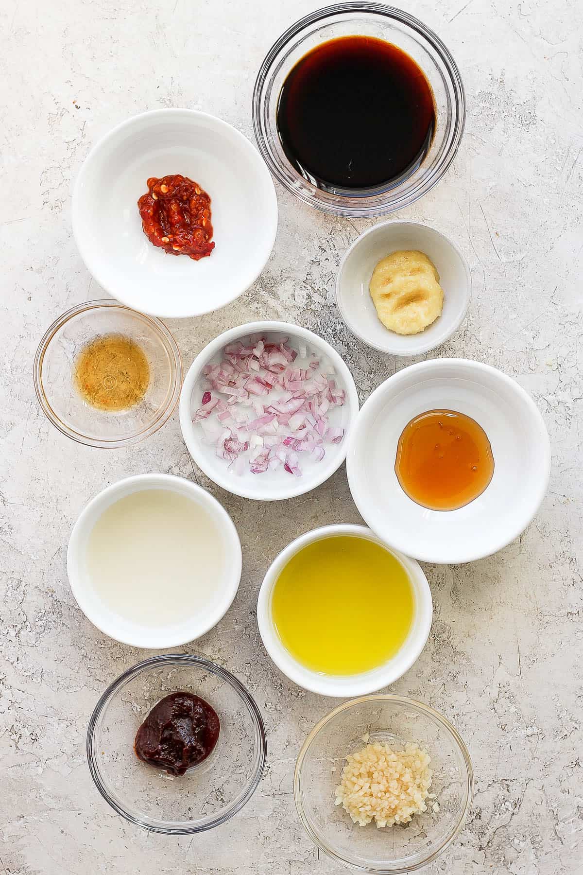 Individual bowls of soy sauce, chili garlic sauce, ginger, shallots, rice wine vinegar, honey, olive oil, sesame oil, garlic, and gochunjung sauce.