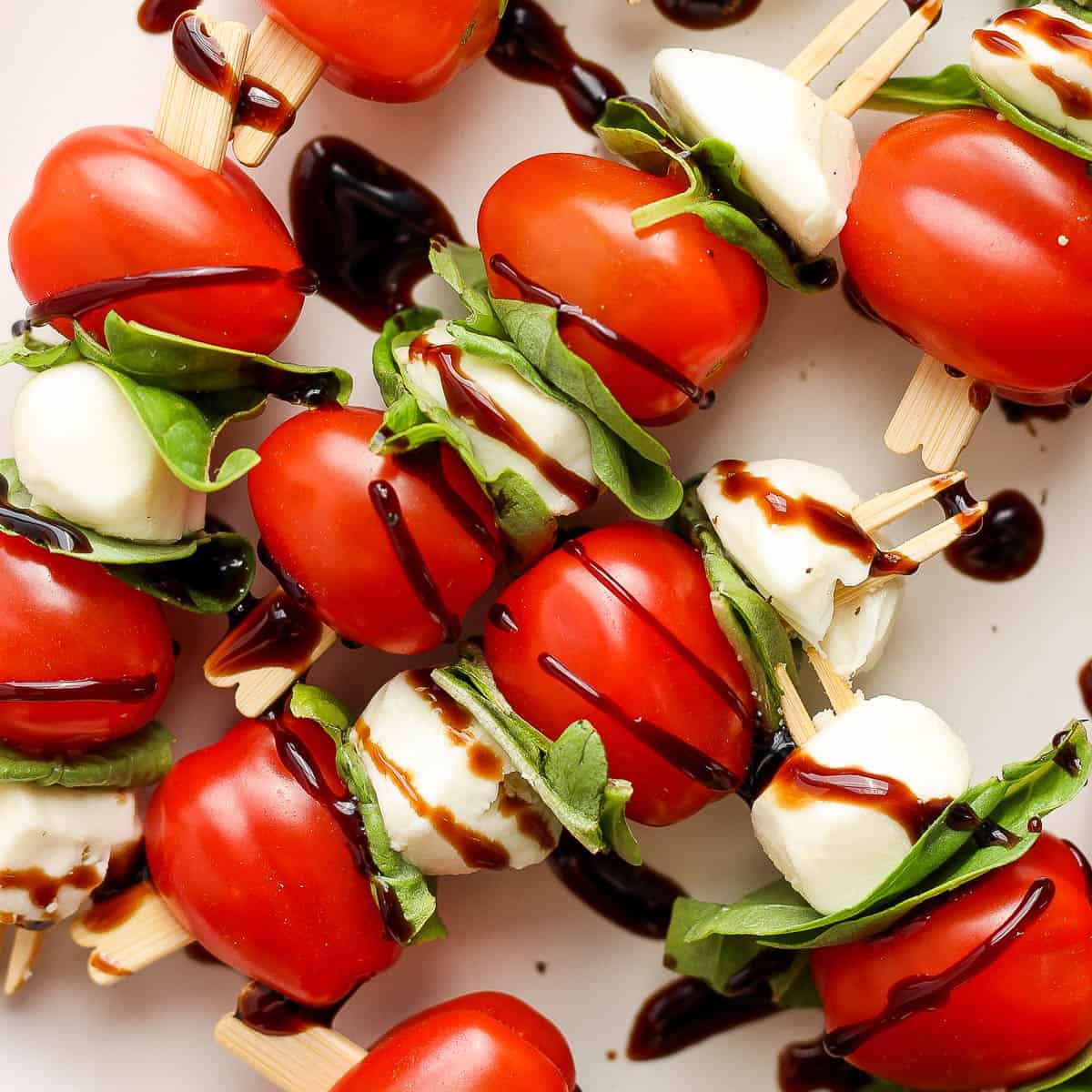 Top down shot of caprese skewers with cherry tomatoes, mini mozzarella balls, fresh basil and balsamic glaze.