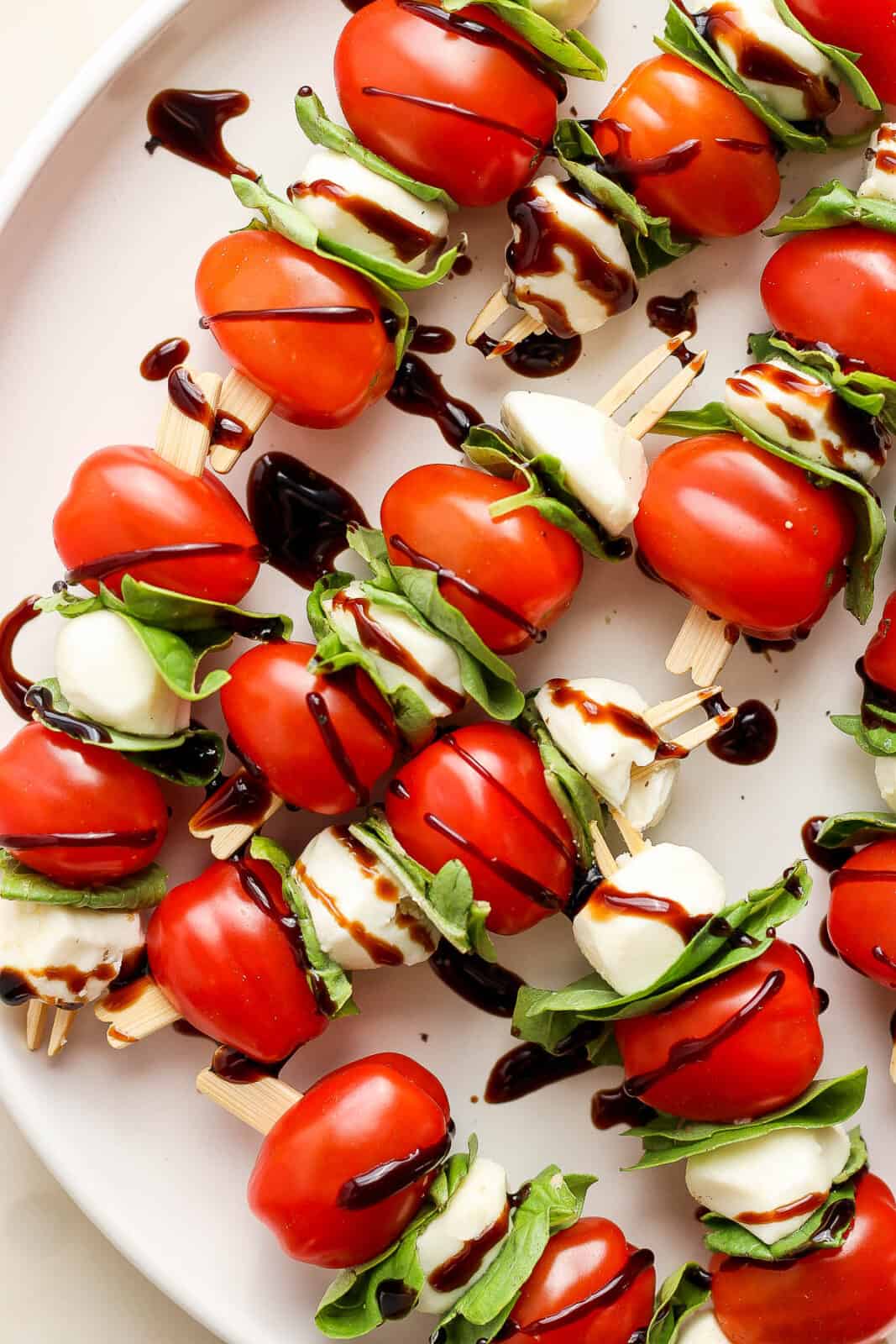 A plate full of caprese skewers with balsamic glaze.