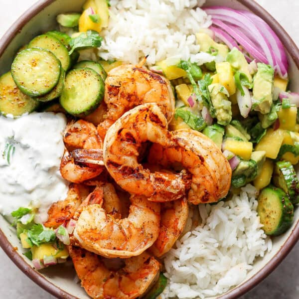 Top down shot of a bowl with rice, grilled chili lime shrimp, mango salsa, cucumbers and red onion.