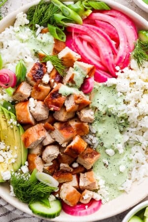 Top down shot of a Green Goddess Bowl with grilled chicken, avocado, pickled onions, dressing and feta.