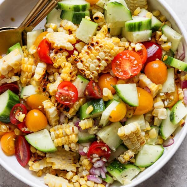 Top down shot of a bowl full of grilled corn salad with corn, tomato, cucumbers, and red onion with a spoon sticking out.