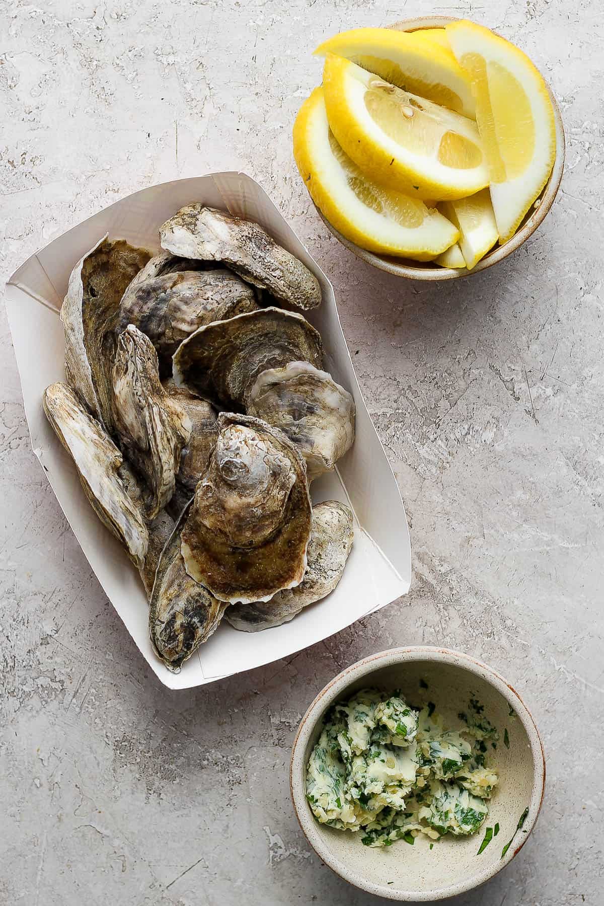 Raw oysters, lemon wedges, and herbed butter in separate bowls.
