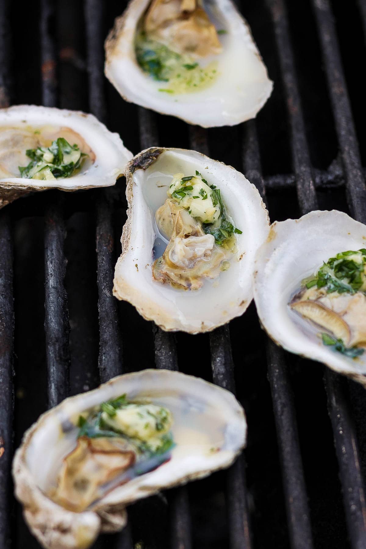 Oyster halves with herby butter in them on the grill grates.