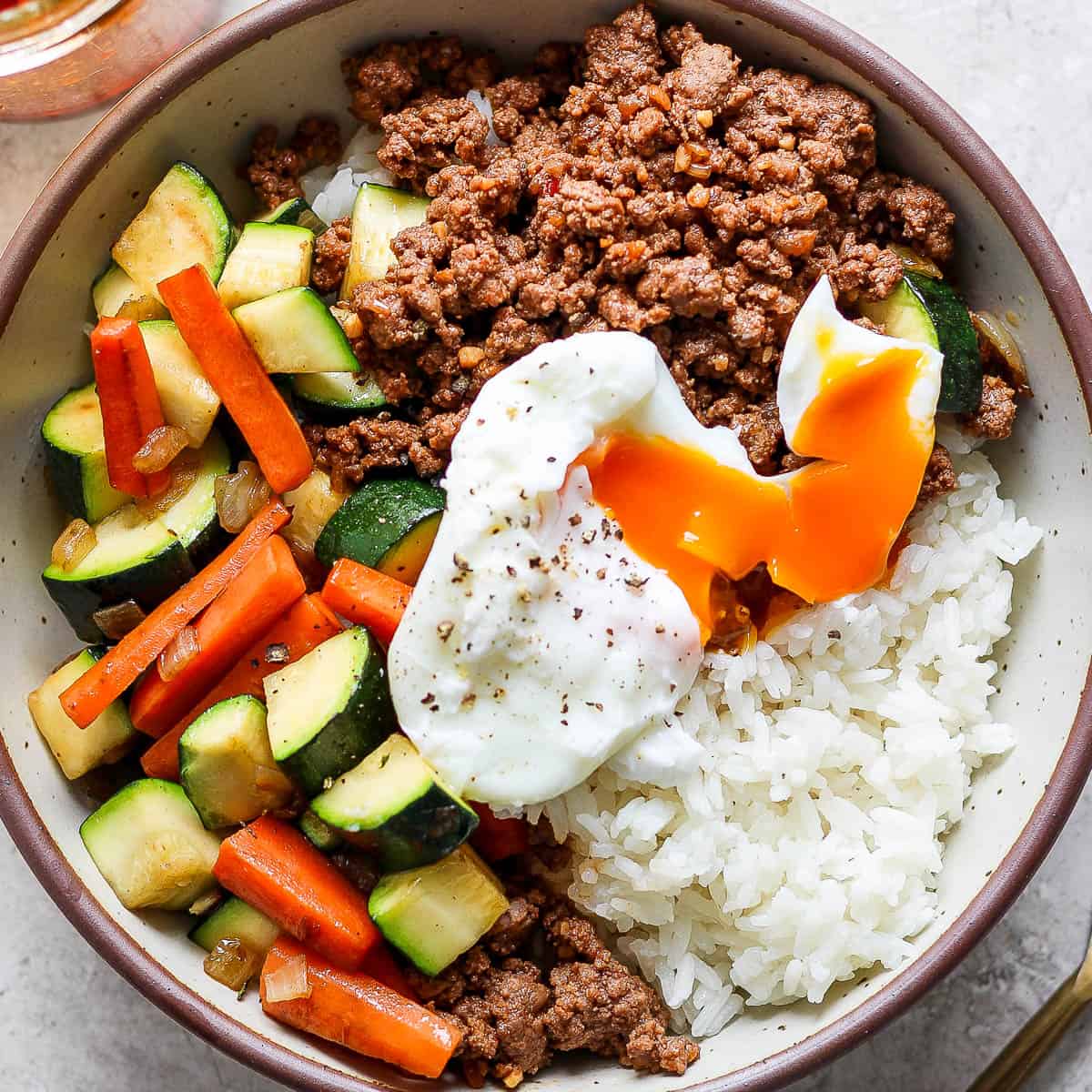 Top down shot of a Ground Beef Rice Bowl with veggies and poached egg on top.