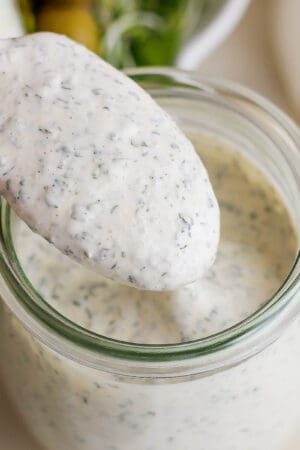 A small jar of homemade ranch dressing with a spoon lifting some out.