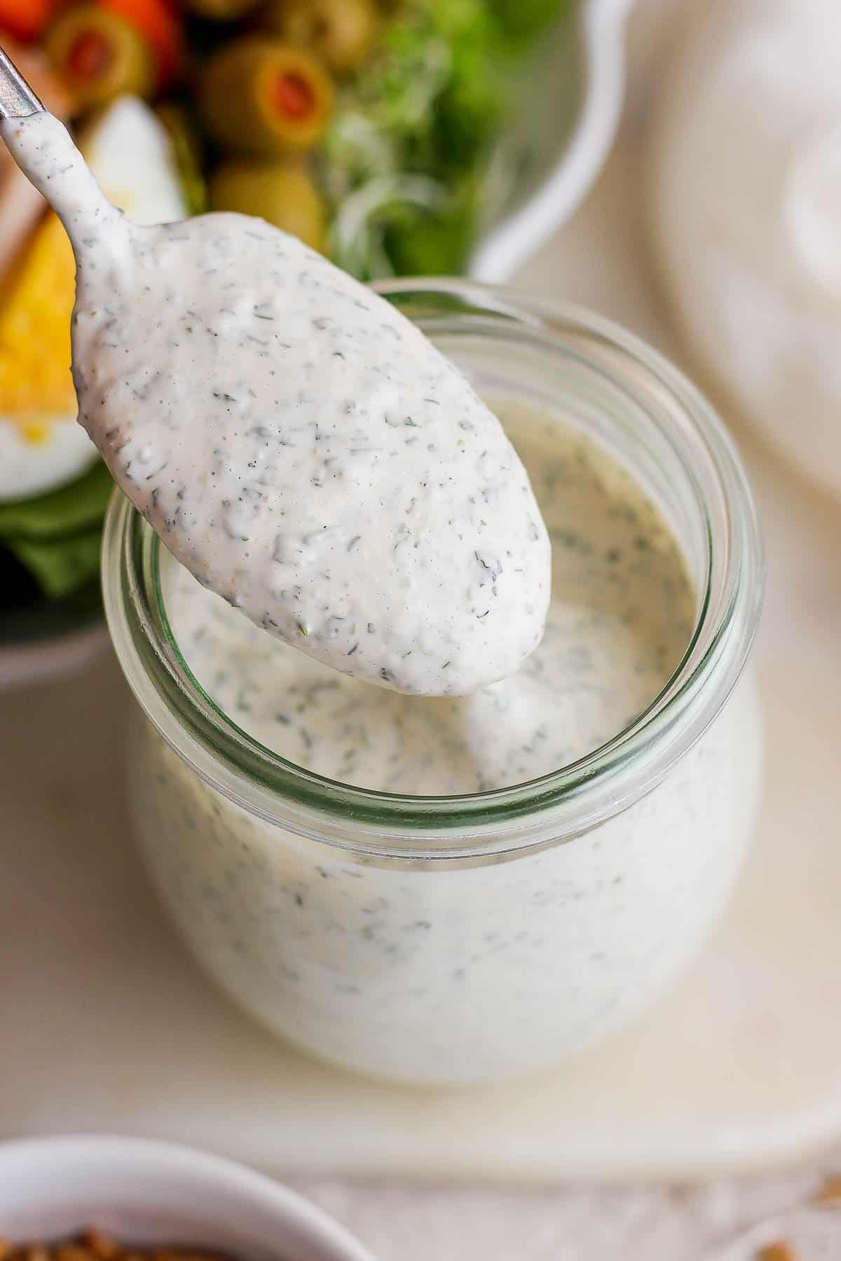 A spoon with ranch dressing on it hovering over a mason jar.