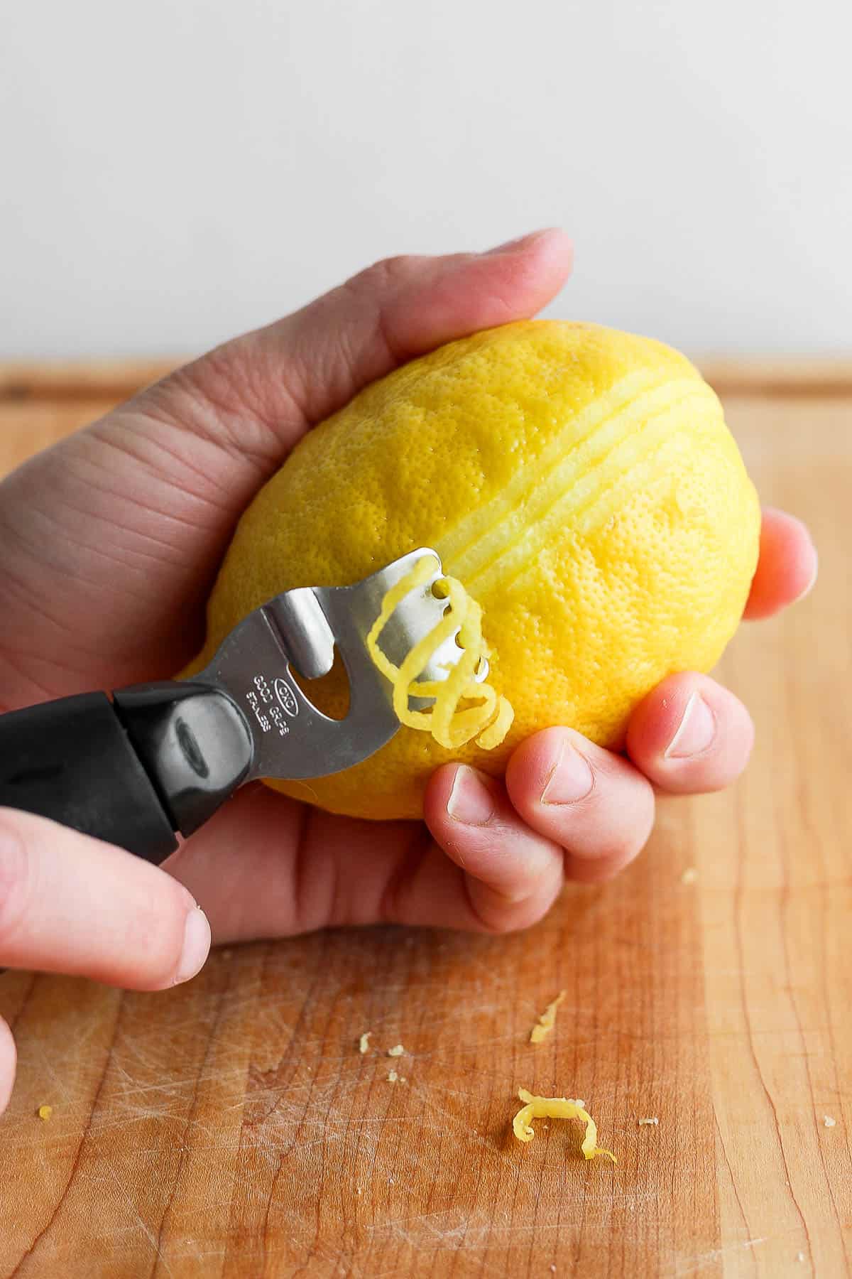 A hand holding a lemon and a zester being pulled down the side.