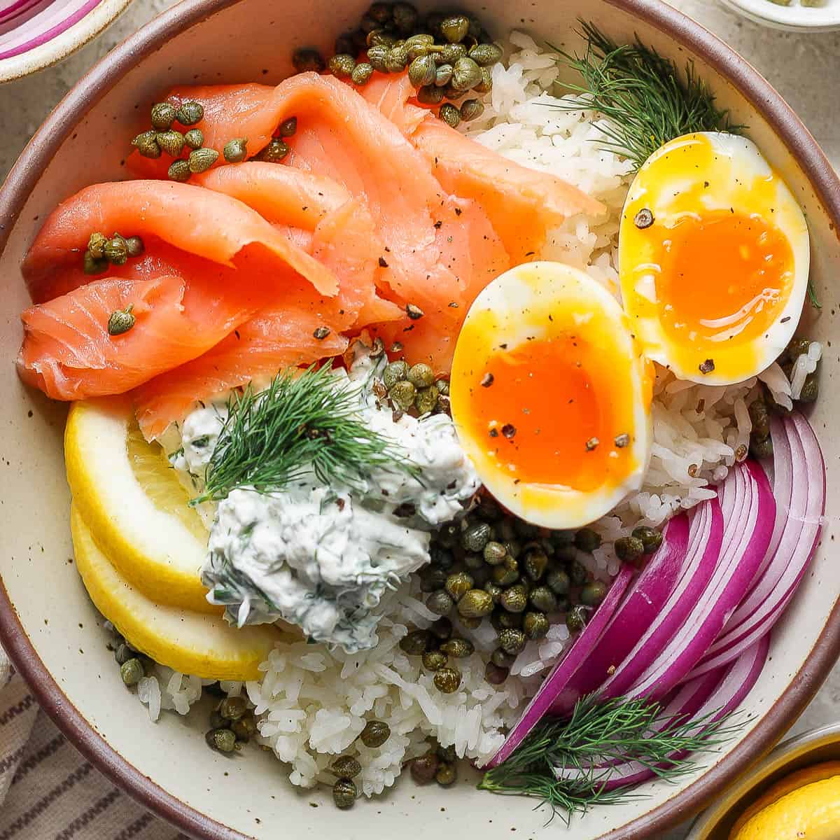 Top down shot of a Lox Bagel Rice Bowl with soft boiled egg, lox, rice, capers and lemon.