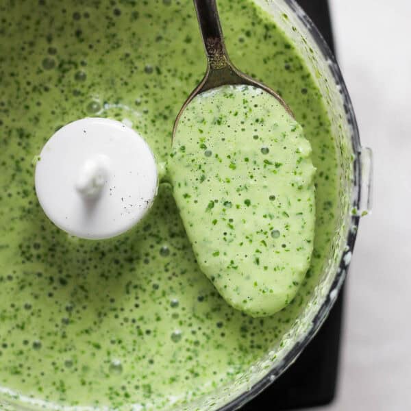 Top down shot of a small food processor full of peruvian green sauce with a spoon pulling some out.