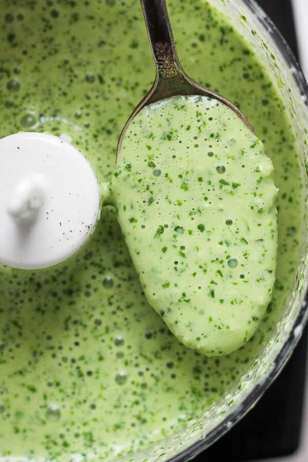 Top down shot of a small food processor full of peruvian green sauce with a spoon pulling some out.