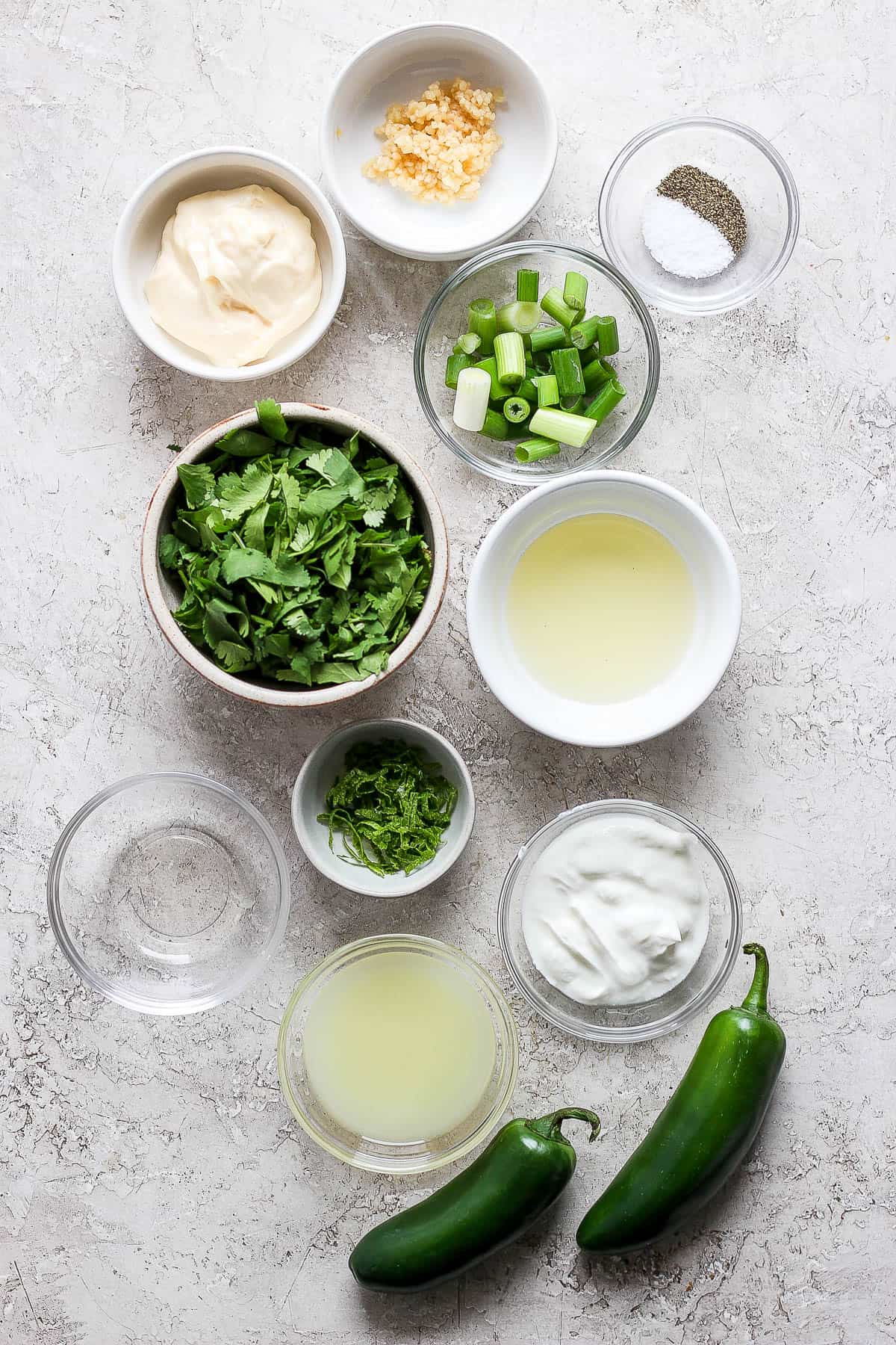 Individual bowls of minced garlic, mayo, green onions, salt & pepper, cilantro, lime juice, greek yogurt, jalepeno, rice vinegar, and olive oil.