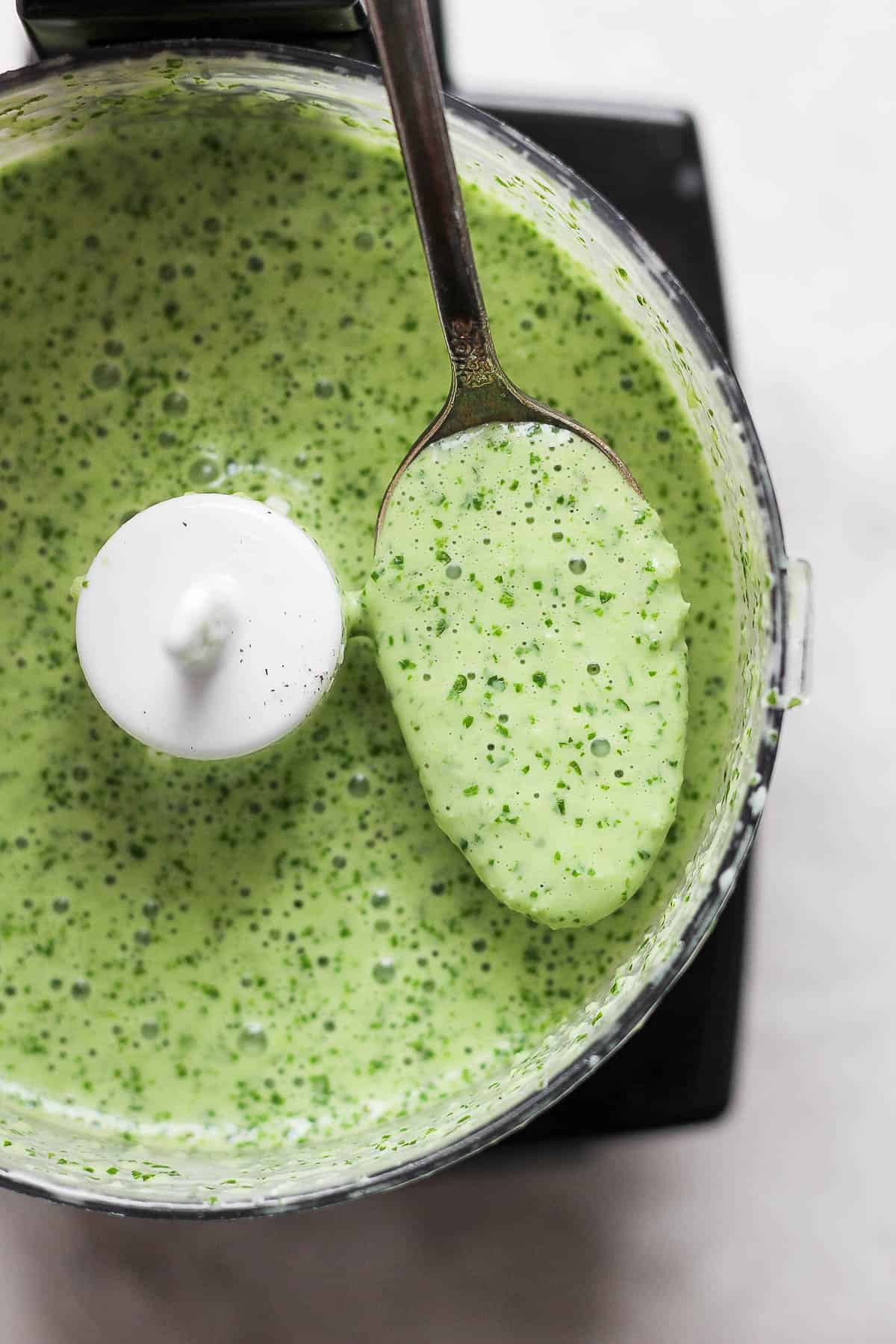 Peruvian green sauce in a food processor with a spoon scooping some up.