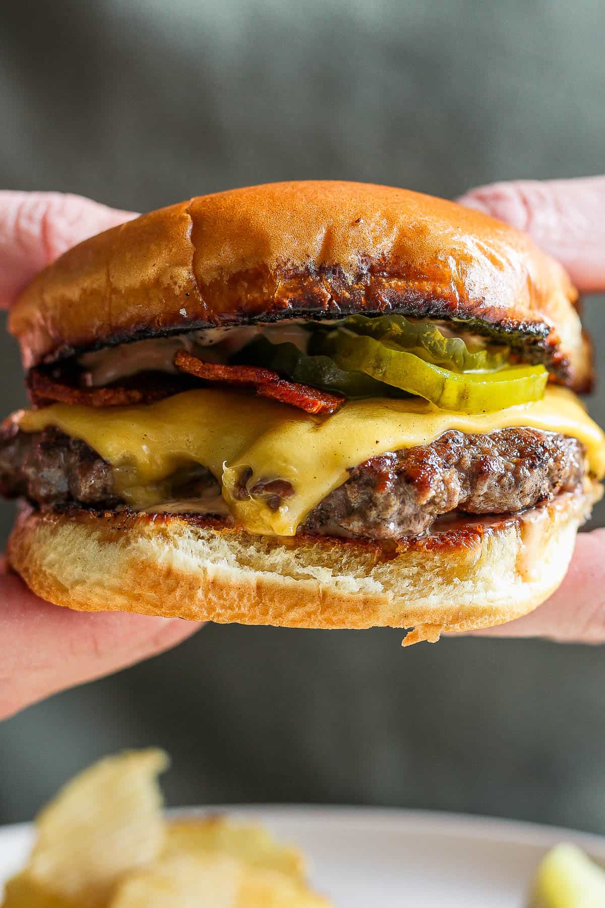 Two hands holding a fully topped smash burger.