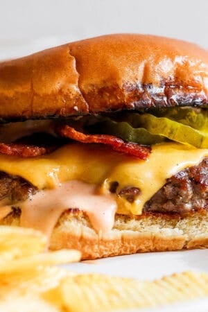 A smash burger on a plate with melted cheese, burger sauce, bacon and pickles on a toasted bun.