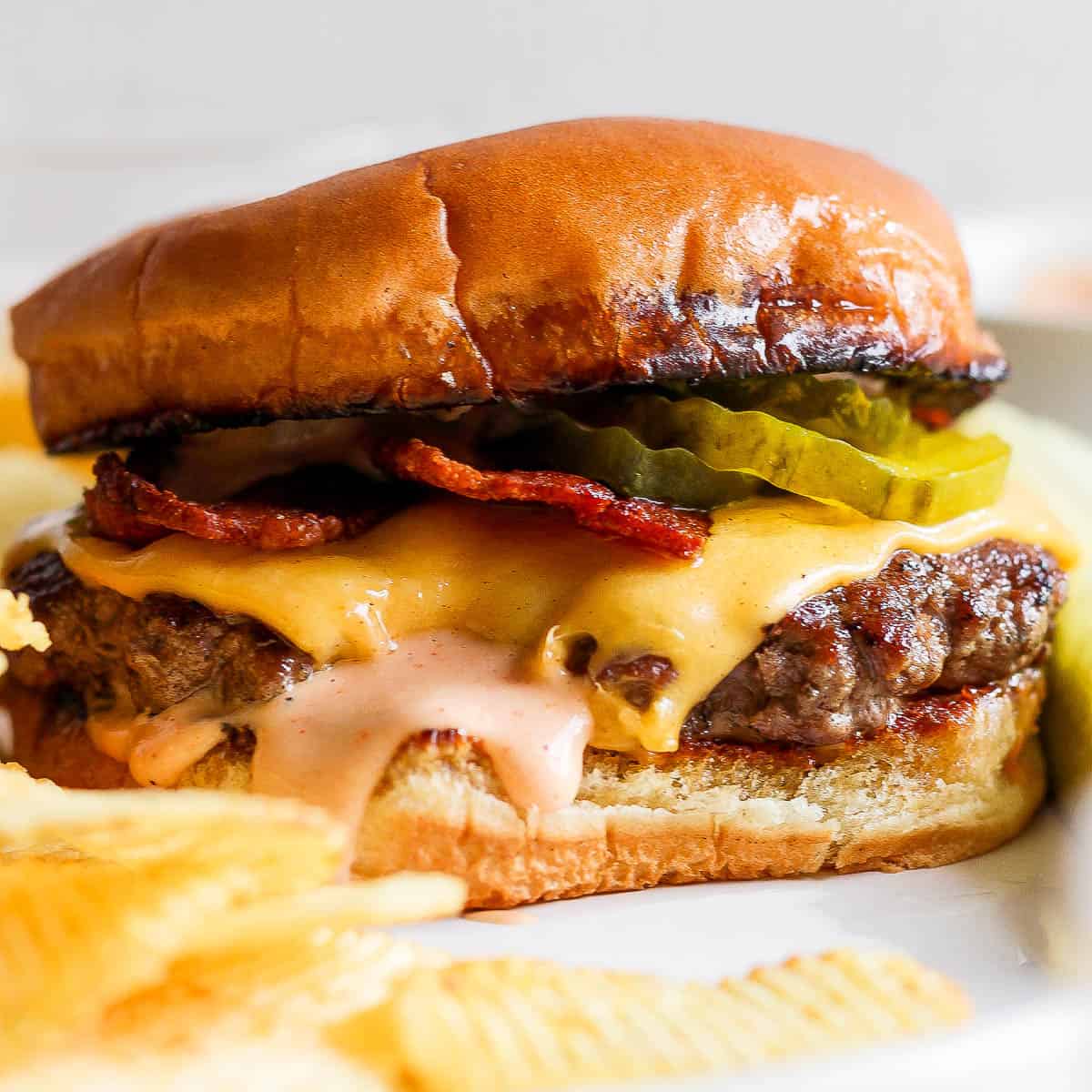 A smash burger on a plate with melted cheese, burger sauce, bacon and pickles on a toasted bun.